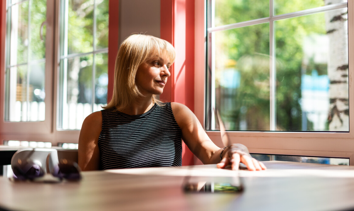 Thoughtful adult mature woman looking through window while sitting at table in cafe. Middle aged woman relaxing.