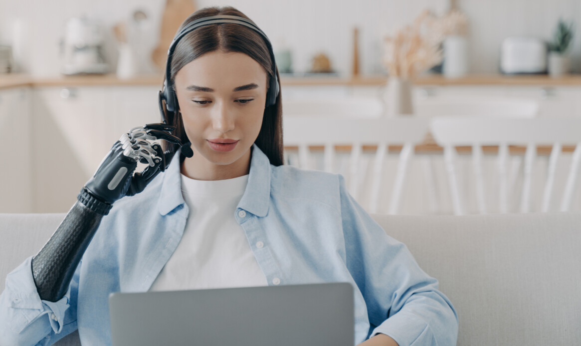 Disabled young woman in headset has online meeting with computer. Remote work.