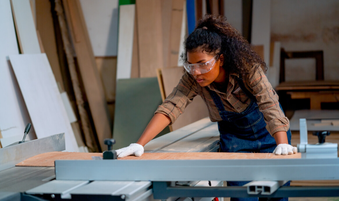 Professional carpenter woman check about cutting machine during work with wood product in workplace.